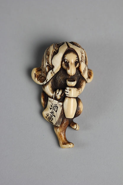 18th-century ivory netsuke of a tanuki with a sake bottle and sake bills, reflecting its comic, convivial image.