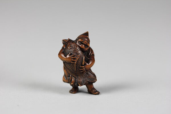 Wooden netsuke, 19th century, of Ebisu in his pointed cap hugging a large fish, his emblem as god of fishermen.