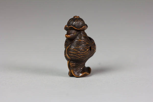 18th-century Japanese netsuke of a tanuki wearing a lotus leaf, recalling the shape-shifting trick of tanuki folklore.