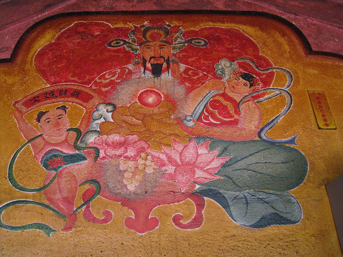Painted temple mural of Caishen enthroned, flanked by attendants, one holding a banner with a wealth-bringing inscription.
