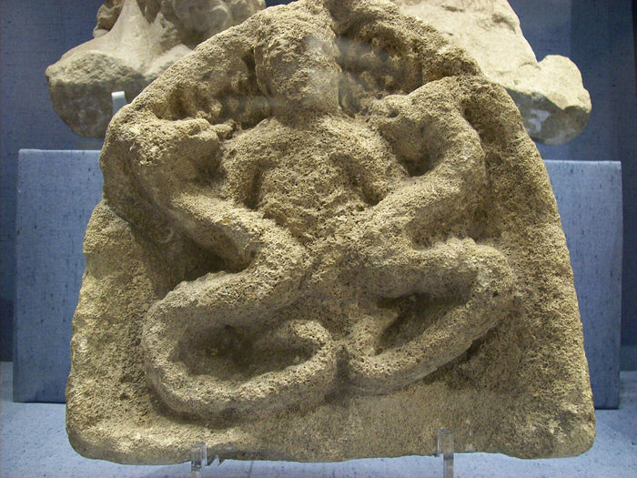 Roman relief at Corinium Museum, Cirencester, showing Cernunnos seated cross-legged with serpents in Roman Britain.