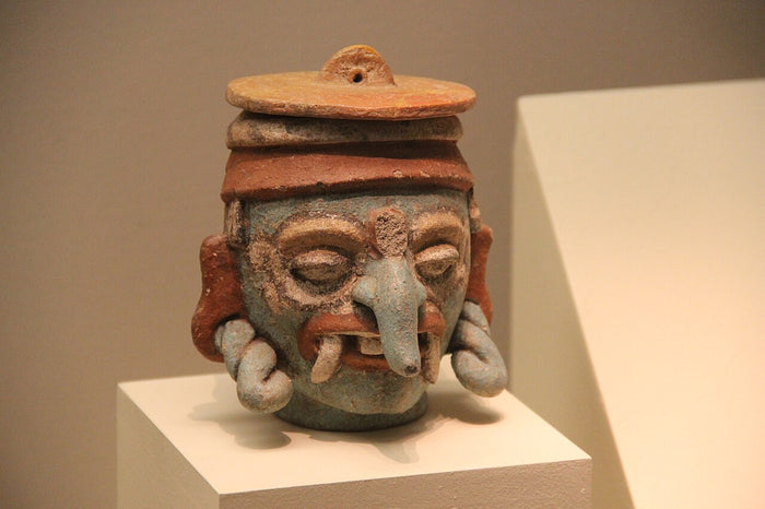 Postclassic Chaak vessel from Mayapan, with the god's long curled nose, fangs and spiral eye rings in blue-painted clay.