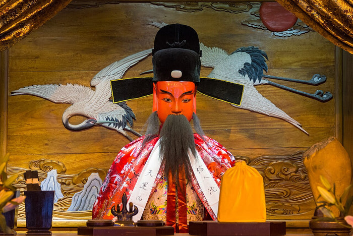 Painted City God figure in official's black hat and embroidered robe before a crane relief, Shanghai City God Temple.