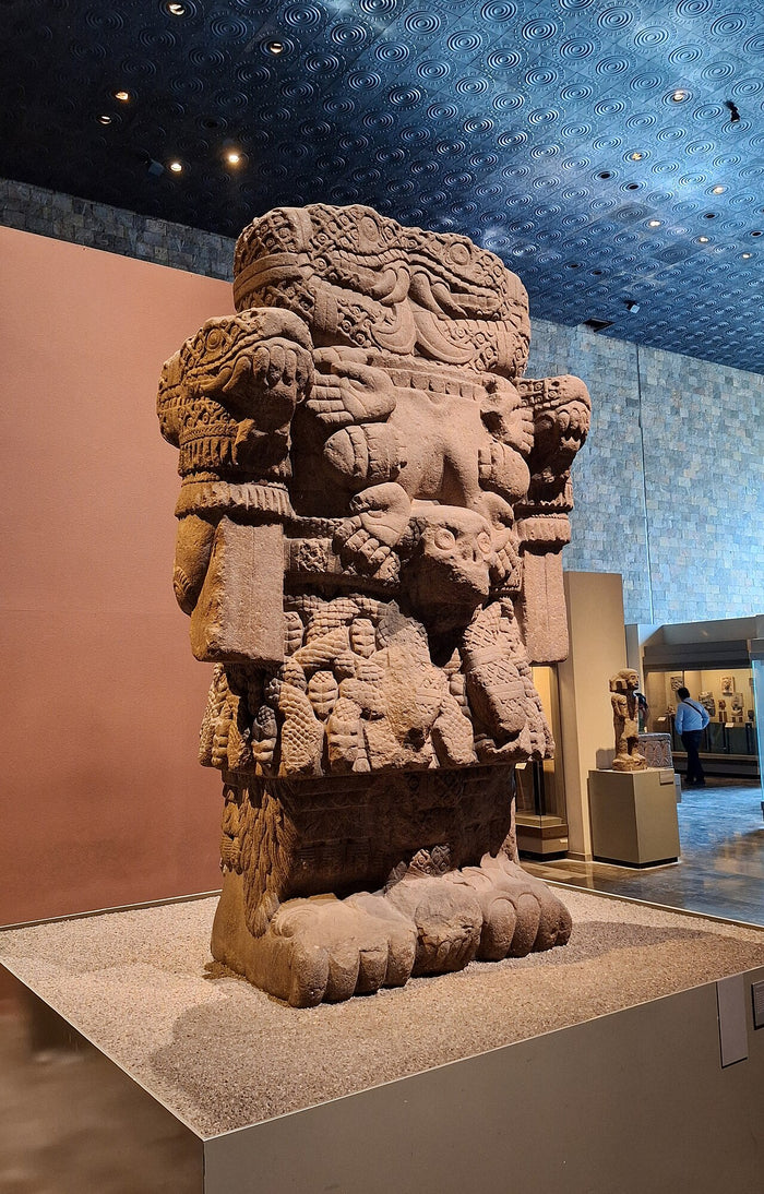 Three-quarter view of the Coatlicue colossus in the museum, showing its massive volume, serpent heads at the shoulders and clawed feet.