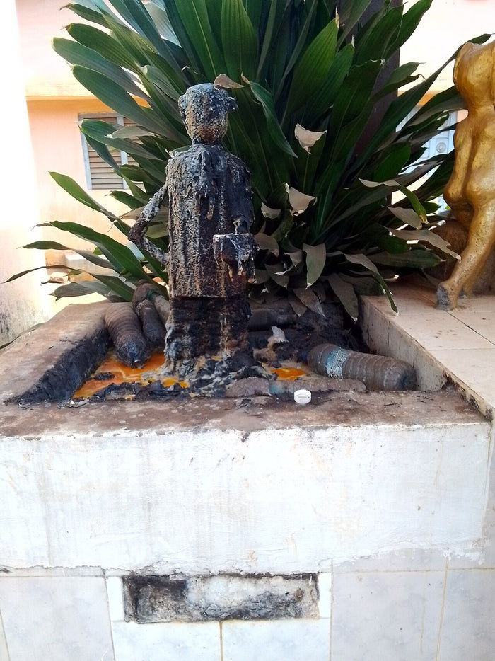 Ogou deity figure at Abomey, 2024, blackened by libations and offerings, showing devotion to the iron orisha in Benin.