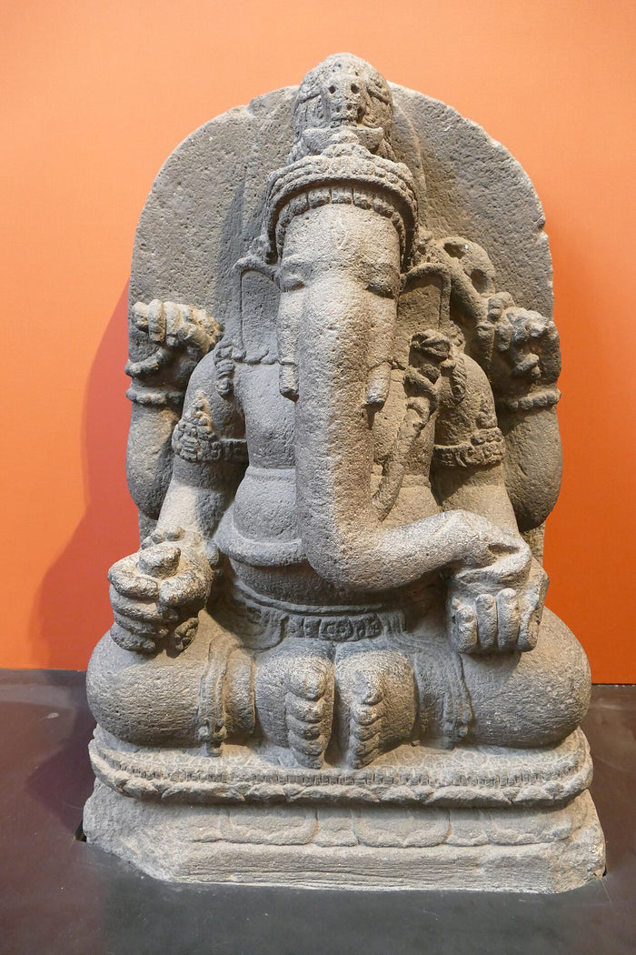 Seated stone Ganesha with elephant head, crown and rounded belly, shown in a museum display.