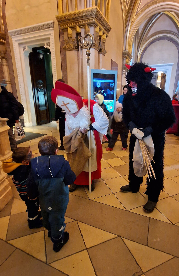 December 2023 Advent custom: Saint Nicholas in bishop's mitre with a black-furred Krampus carrying a birch bundle, greeting children indoors.