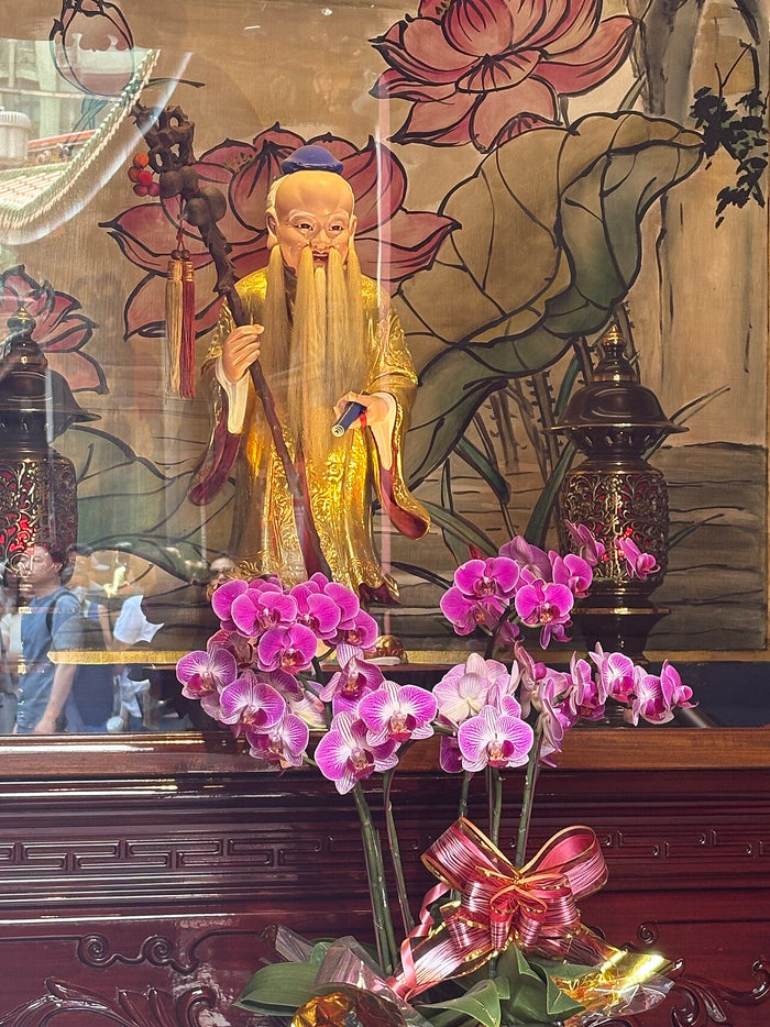 Gilded Yue Lao figure at Bangka Longshan Temple, Taipei. He has a long white beard and a staff, and orchids stand before him.