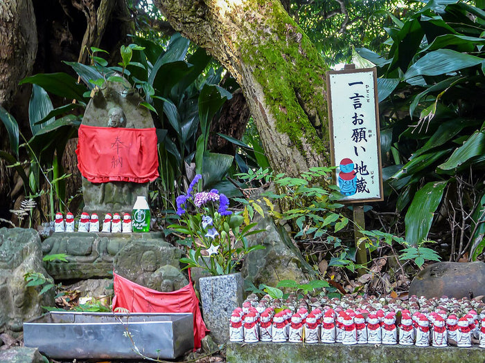 Wish-granting Jizō with red cloth and many small Jizō figurines offered by worshippers at a shrine.