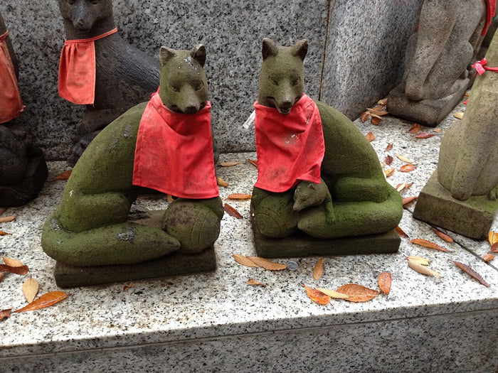 Pair of stone fox statues (kitsune) in red bibs, Inari's messengers, one with a cub.
