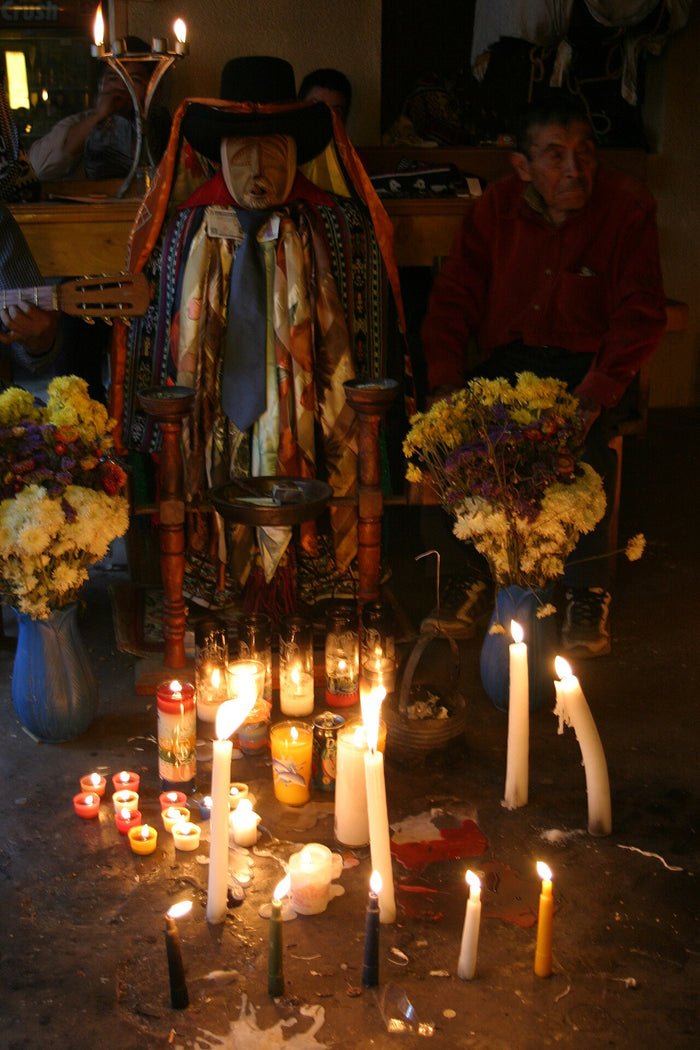 Maximón near Lago Atitlán: wooden mask, hat, layered scarves and ties, with candles and flowers as offerings.