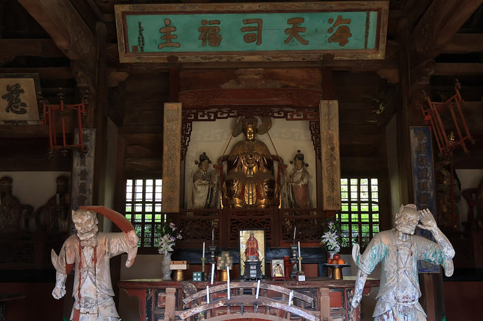 Interior of a Mazu temple with the central enthroned goddess, attendants and guardian figures beneath the 'Hai Tian Si Fu' plaque.