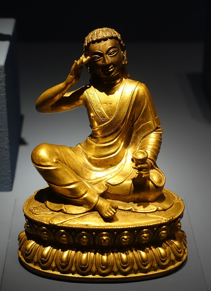 Gilt bronze statue of Milarepa seated, right hand at his ear in the singing gesture, holding a cup.
