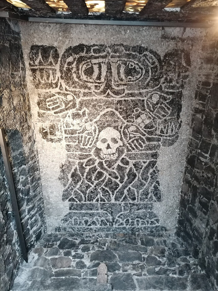 Mosaic depicting Coatlicue's figure, with skull and serpent skirt, set in a stone-walled niche as a modern homage.