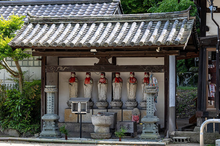 Roofed temple shelter housing a row of Jizō statues in red bibs, with stone lanterns.