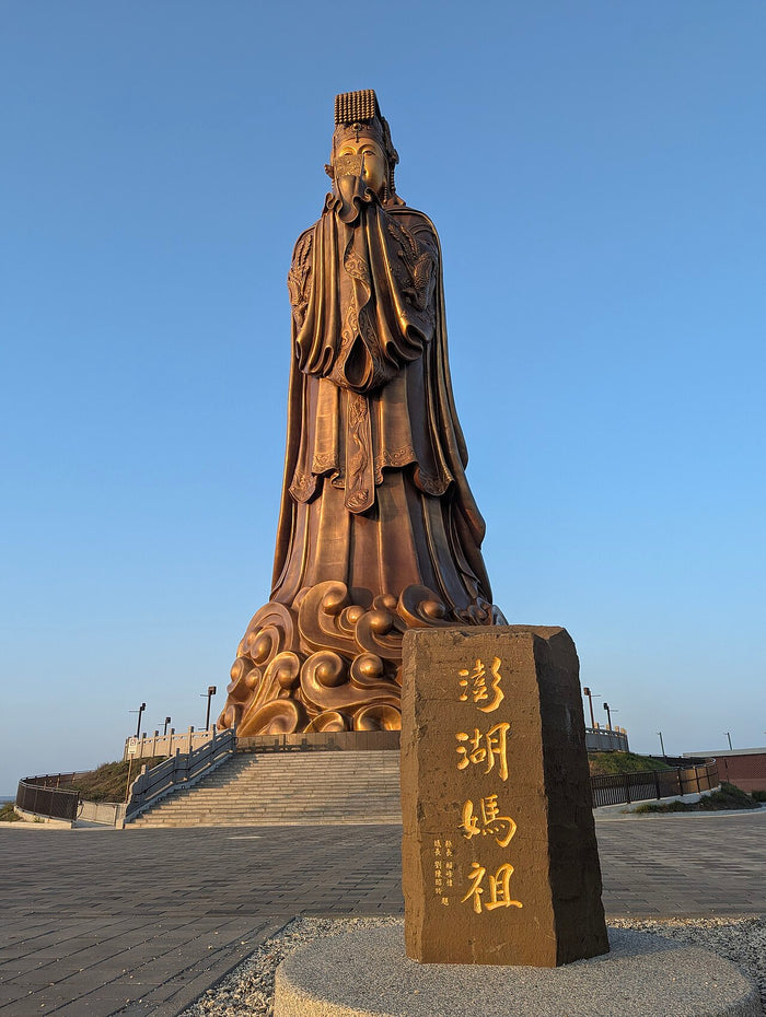 Monumental bronze Mazu statue at Penghu, standing on carved waves and facing the sea she protects.