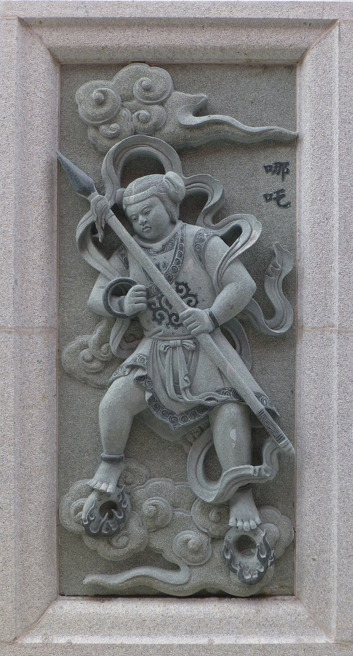 Granite relief of Nezha at Ping Sien Si, shown as a child warrior with spear, armlet ring and fire-wheels under his feet.