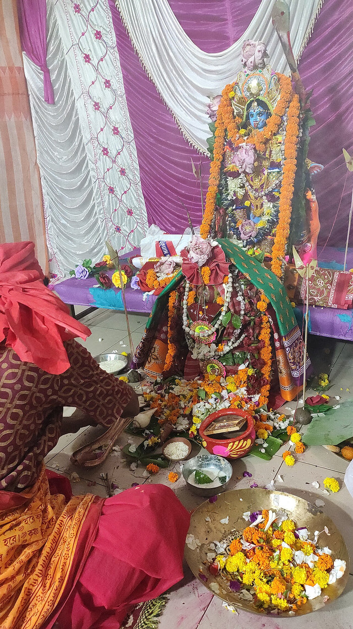 Household Kali Puja, 2025: a blue-faced Kali image dressed in marigold garlands, with offerings and a worshipper.