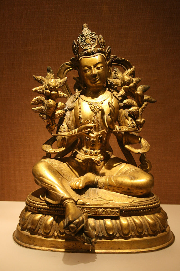 Qing-dynasty gilt bronze Green Tara seated in royal ease, flanked by two flowering lotus stems.