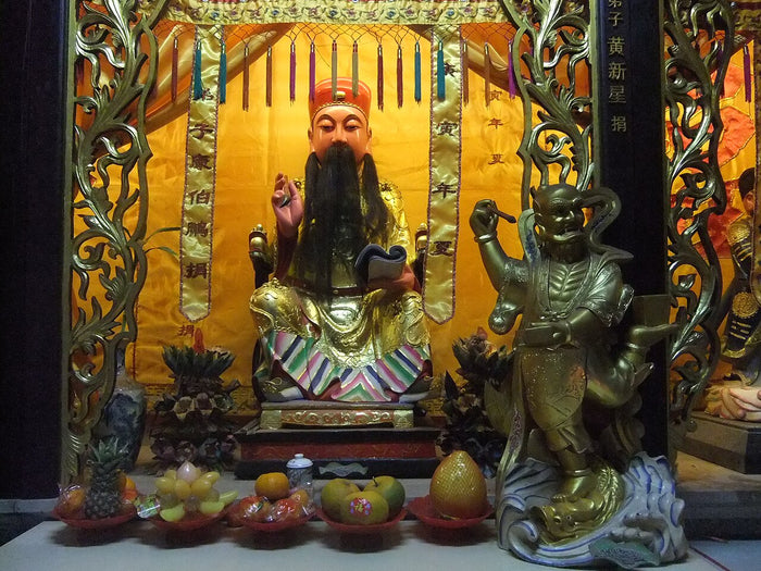 Seated Tudi Gong statue with long white beard and official's hat, flanked by offerings of fruit, at Quanshan, Quanzhou (2012).