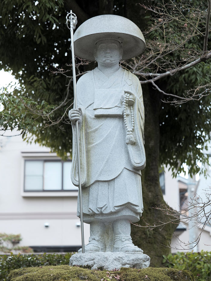 Stone pilgrim statue of Kōbō Daishi with broad hat, staff and prayer beads, the standard Shikoku pilgrimage image.
