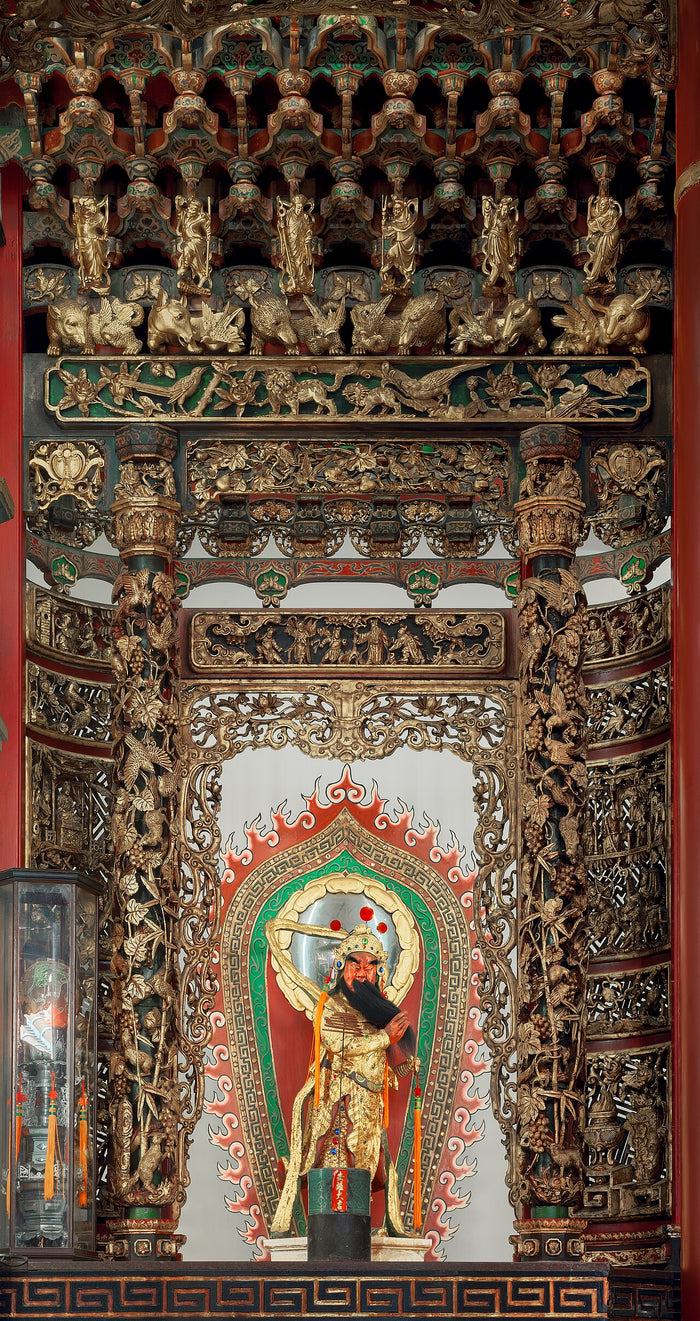 Shrine statue of Guan Gong with red face and long beard, framed by gilded carved dragon pillars and woodwork.