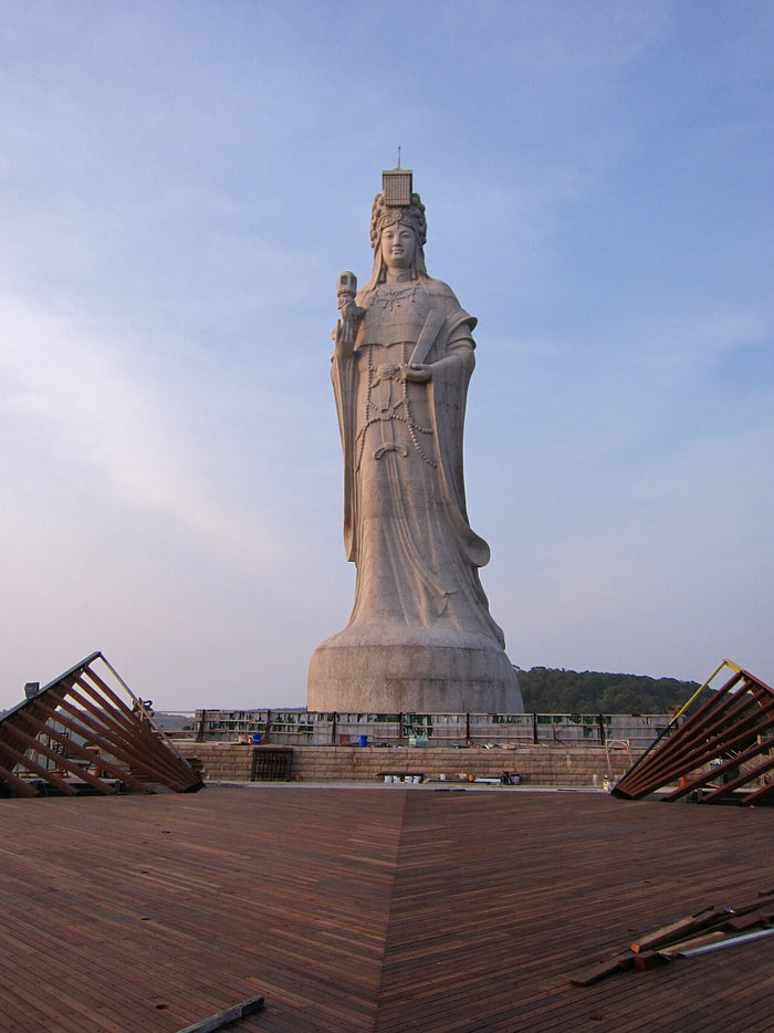 Giant granite Mazu statue holding a ceremonial tablet, shown from the front on its stone base.