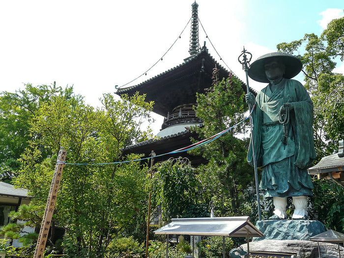 Statue of Kōbō Daishi as a pilgrim beside a pagoda at a temple, marking his Shikoku pilgrimage.