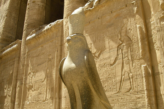 Granite falcon statue of Horus wearing the double crown before the Temple of Edfu's carved wall.