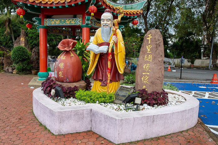 Yue Lao statue at Thean Hou Temple, Kuala Lumpur. He holds a book and staff, with a large red bag beside him.
