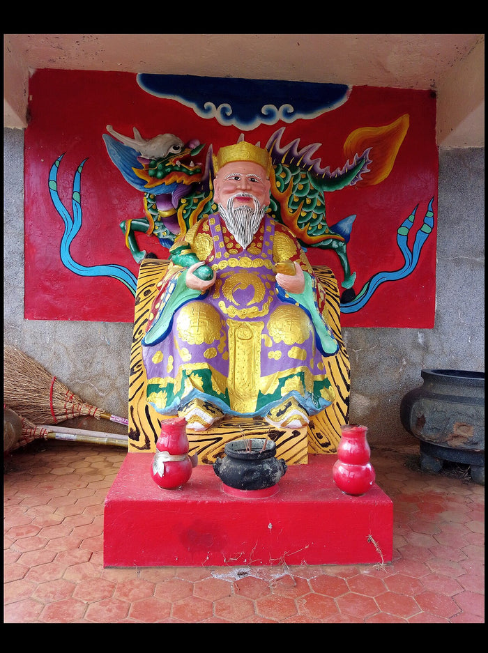 Colourful painted Tudi Gong statue seated before a mural of a qilin-like beast, with incense burner and offerings.
