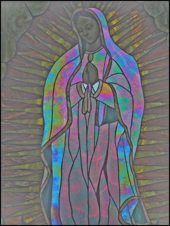 Stained-glass depiction of Our Lady of Guadalupe with praying hands and radiant mandorla, showing the image's use in church art.