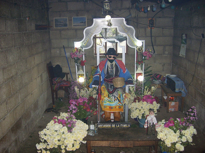 San Simón shrine in Zunil: the figure sits in a hat and bright clothes among flowers and lights.