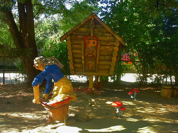 Park figure of Baba Yaga in her mortar beside the hut on chicken legs, with fly-agaric mushrooms.