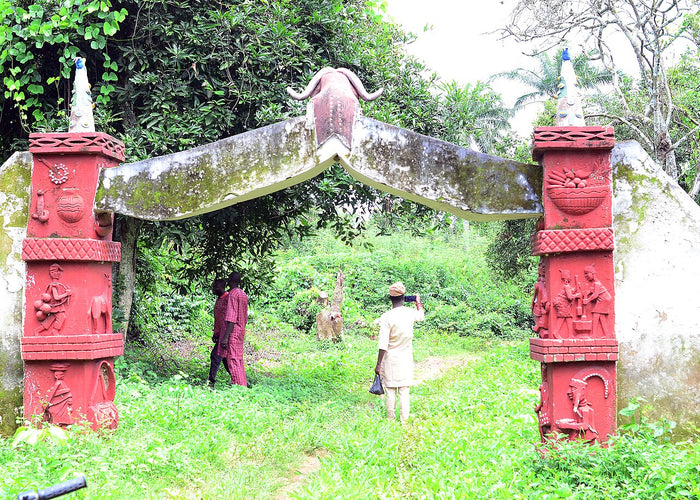 Red entrance gate of Oya Grove with carved figures and a buffalo-horn crest, evoking Ọya's buffalo association.