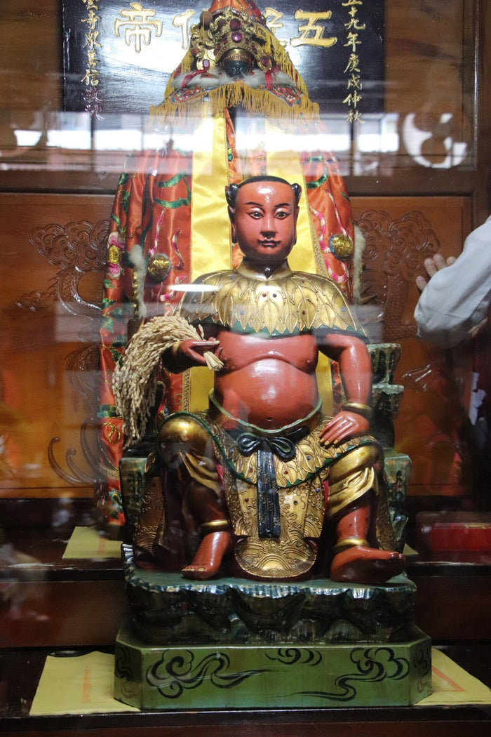 Seated Shennong statue at Taipei Qingyun Temple holding a sheaf of grain, an emblem of his role as divine farmer.