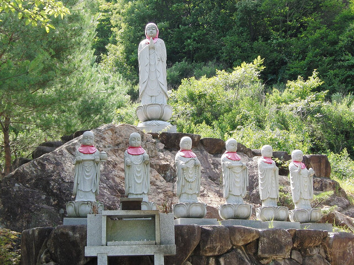 Row of stone Jizō statues on lotus pedestals wearing red bibs, a common devotional practice.