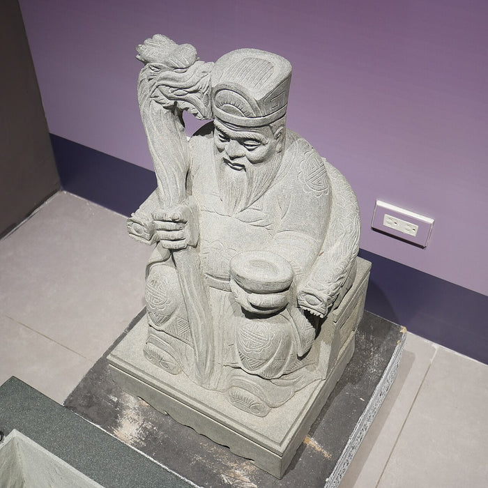 Stone Tudi Gong sculpture with dragon-headed staff and ingot bowl, displayed at the Taoyuan Tudigong Cultural Museum (2020).