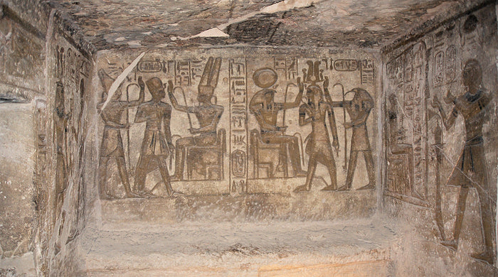 Abu Simbel chamber relief: falcon-headed, sun-disc-crowned Ra enthroned beside other gods and the king.