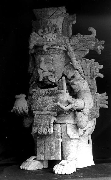 Large ceramic figure of Chaac holding vessels, with his characteristic long, pendulous snout and elaborate headdress.