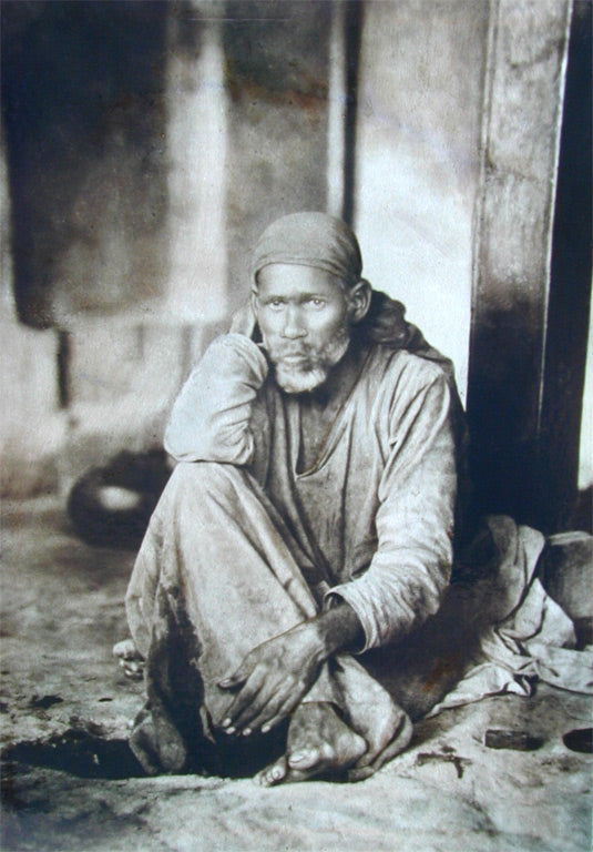 Sai Baba seated in a contemplative pose, resting his head on his hand, in a photograph from before 1918.