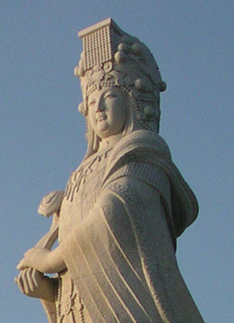 Large white stone statue of Mazu in a flat-topped crown with hanging beads and flowing robes.