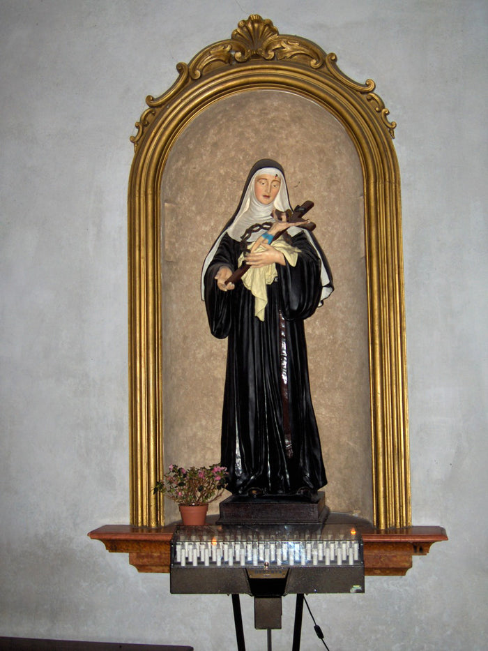 Painted statue of St Rita in Augustinian habit holding a crucifix, with a mark on her forehead, in a gilded niche.